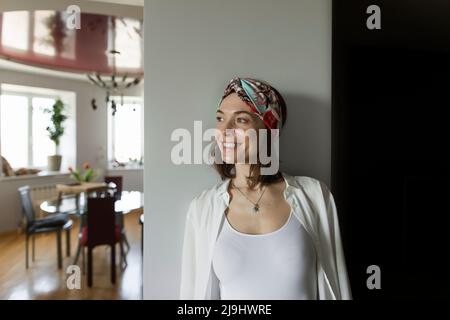 Lächelnde, reife Frau, die zu Hause ein Stirnband an der Wand trägt Stockfoto