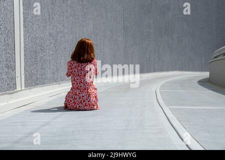 Traurige einsame Frau, die auf dem Fußweg sitzt Stockfoto
