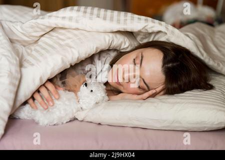 Ältere Frau mit Teddybär schläft zu Hause auf dem Bett Stockfoto