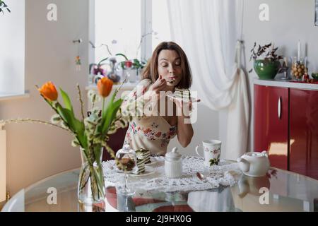 Glückliche Frau, die ein Stück Kuchen am Esstisch isst Stockfoto