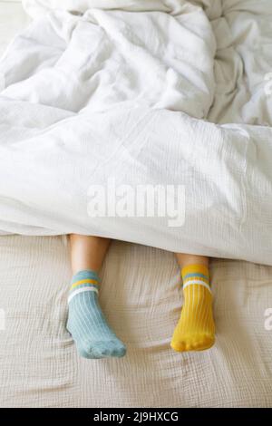 Frau trägt blaue und gelbe Socken im Bett Stockfoto