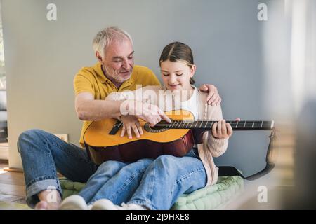 Glücklicher älterer Mann, der Enkelin zu Hause Gitarre unterrichtet Stockfoto