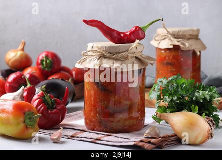 Gemüsesalat mit Auberginen, Karotten, Paprika, Zwiebeln und Tomaten in Gläsern auf hellgrauem Tisch Stockfoto