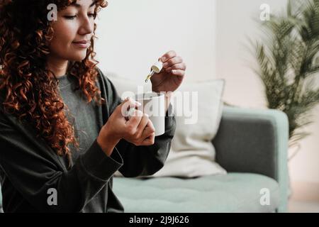 CBD-Hanföl - Frau, die Cannabisöl in einer Teetasse nimmt - Fokus auf die Hand, die einen Droppler hält Stockfoto