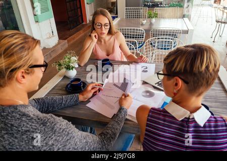 Eine Gruppe von drei stilvollen freiberuflichen Studenten Unternehmer in Mode gut gekleidet arbeiten am Tisch mit Laptop in einem Sommer-Café im Freien sitzen Stockfoto