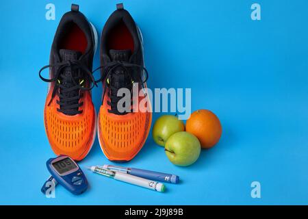 Orangefarbene Sneakers, Früchte, Glucometer und Insulin-Spritzenstifte auf blauem Hintergrund Stockfoto