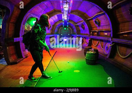 Frau spielt auf der Minigolfbahn Ocean Adventurer in Mr Mulligan's Lost World, Stevenage, Hertfordshire, Großbritannien Stockfoto