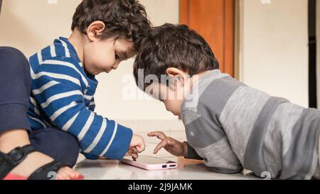 Zwillingkinder, die mit dem Handy auf dem Boden ihres Heims spielen Stockfoto