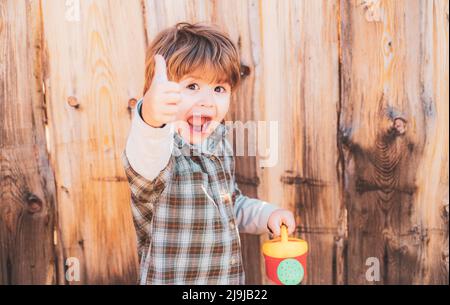 Glückliches Kind mit Schaufel und Gießkannen. Niedlicher kleiner Junge, der Blumen im Frühlingsgarten wässert. Gartengeräte. Stockfoto