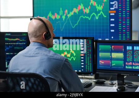 Rückansicht eines unkenntlich reifen kaukasischen Mannes, der Kopfhörer trägt und die Börsenhandelsstatistiken überwacht Stockfoto
