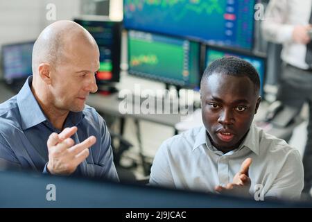 Ein Blick aus der Perspektive zweier ethnisch unterschiedlicher Männer, die im Aktienhandel und in Investmentgesellschaften arbeiten und Charts und Grafiken betrachten und diskutieren Stockfoto