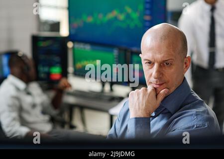 Reifer kaukasischer Mann, der am Aktienmarkt arbeitet und im Büro Charts und Grafiken der Währung auf dem Monitor beobachtet Stockfoto