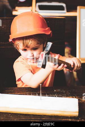 Kind mit Helm in orange Hut. Werkzeugbau. Hämmerte Junge. Kid Hämmer Nagel. Stockfoto