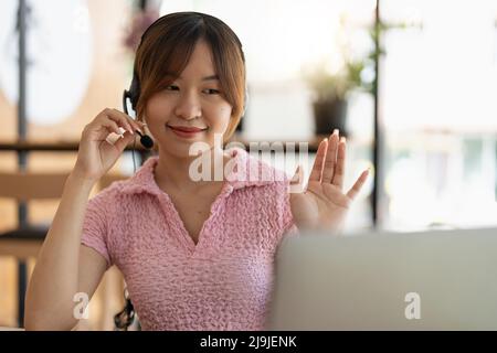 Lächelndes Mädchen Student tragen drahtlose Kopfhörer Studie online mit Lehrer, glücklich junge asiatische Frau lernen Sprache hören Vortrag sehen Webinar schreiben Stockfoto