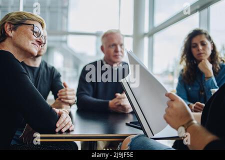 Geschäftsführerin, die auf die Vertragsdiskussion im Sitzungssaal achtet, Geschäftsleute sitzen an einem runden Konferenztisch für ein Meeting mit Stockfoto