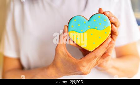 Frau hält herzförmige Lebkuchenkekse mit ukrainischen Flaggen Farben in den Händen Stockfoto