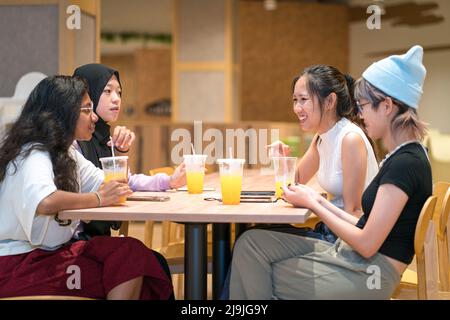 Eine Gruppe von vier jungen asiatischen Frauen, die eine tolle Zeit in einem Café haben. Orangensaft trinken und gemeinsam plaudern. Stockfoto