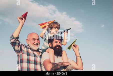 Glückliches Kind spielt im Freien. Glückliche Mann Familie viel Spaß zusammen. Kinder, die an sonnigen Tagen mit einfachen Papierflugzeugen spielen. Vater gibt Sohn fahren auf dem Rücken Stockfoto