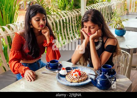 Traurige modische indische Freunde Paar von zwei Frauen, die cakes.friends lang erwartete Treffen Klatsch Studenten essen Pfannkuchen trinken Masala Tee zu sehen Stockfoto