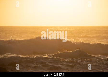 Warmer Sonnenuntergang über krachenden Meereswellen Stockfoto