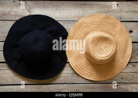 Schwarzer Hut und Strohhut auf Holztisch, zwei verschiedene Hüte, Mode und Schönheit Stockfoto