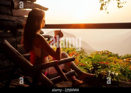 Schöne Frau mit einer Tasse Kaffee Tee genießen die Aussicht vom Balkon auf Teeplantage Dschungel in Indien Kerala Goa wildernest Natur Spa Resort Stockfoto