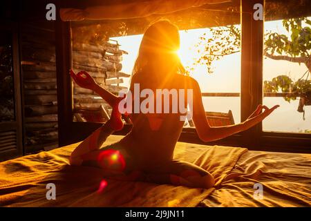 Frau in tropischen offenen Yoga-Studio platzieren Sie einen Blick auf die Hügel, während Sonnenuntergang.Mädchen in Öko-Hotel Panoramafenster genießen Einsamkeit mit der Natur Stockfoto