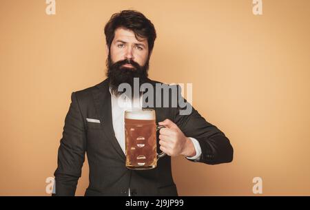 Bärtiger Mann in schwarzem Anzug mit einem Glas Bier. Fröhlicher eleganter Mann, der Bier trinkt. Bierkneipen und Bars. Bärtiger Mann trinkt Lagerbier. Stockfoto
