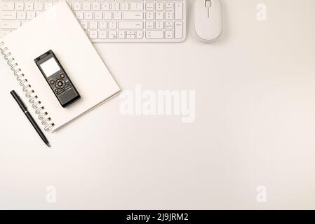 Weiße Tastatur, Maus und Notizblock auf der linken Seite mit schwarzem Stift und Voice Recorder. Fett lag auf weißem Hintergrund mit Kopierplatz. Stockfoto