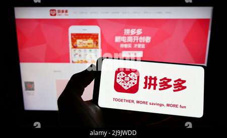 Person, die Smartphone mit dem Logo des chinesischen E-Commerce-Unternehmens Pinduoduo Inc. Auf dem Bildschirm vor der Website hält. Konzentrieren Sie sich auf die Telefonanzeige. Stockfoto