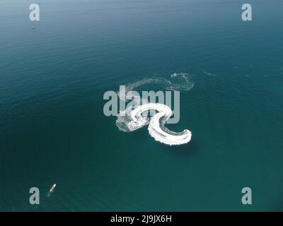 Luftaufnahme von oben nach unten von Wasserschaumspuren mit schönem tiefblauen Schatten des Ozeans. Schöne weiße Spur auf der ruhigen Meeresoberfläche hinter einem kleinen mächtigen Stockfoto