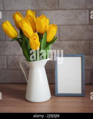 Schöne gelbe Tulpenblumen und leerer Bilderrahmen auf dem Tisch in der Küche Stockfoto