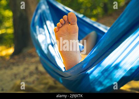 Kinderfuß in einer Hängematte, rollend im Wald im Sommer in der Sonne, Rest in einer Hängematte, ein Fuß in einer Hängematte, Rest im Wald Stockfoto