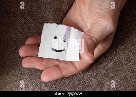 Ein fröhliches Emoticon wird in den Händen einer Frau auf ein Blatt Papier gezeichnet, gute Laune, Freude und ein Lächeln Stockfoto