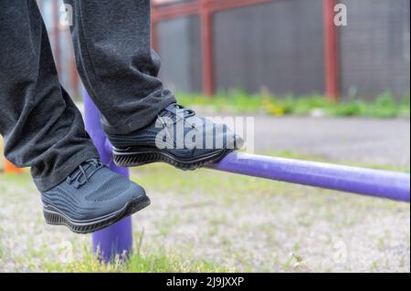 Der untere Teil eines reifen Mannes, der auf einem Outdoor-Sportplatz trainiert. Die Beine eines Mannes, der sich auf Sportschuhen ausstreckt. Gymnastische Übungen. Stockfoto