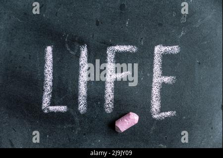 Leben. Ein Wort, das in rosa Kreide auf einer schwarzen Tafel geschrieben ist. Handgeschriebener Text. Daneben hängt ein Stück farbige Kreide. Stockfoto