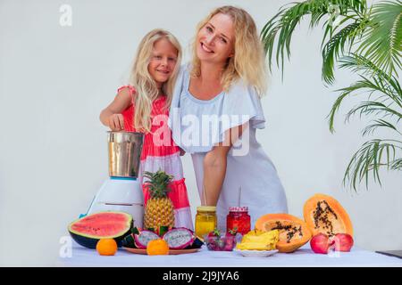 kaukasische Familie in der Küche während des Frühstücks zu Hause. Zwei blonde Schwestern Kochen Smoothies in einem Mixer.Tropical Sommer Thema.Small Business Gemüse Stockfoto