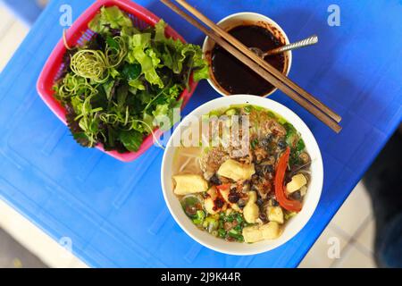 Nahaufnahme von Schneckennadelnudeln (vietnamesisch:Bún ốc) wird auf einem Plastiktisch serviert. Konzept des orientalischen Street Food in asiatischen Ländern. Stockfoto