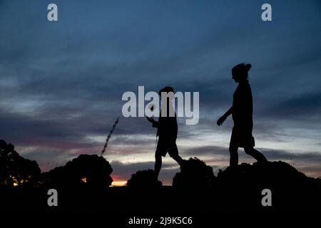 Mutter und Sohn mit einem Ball, der unter dem Abendhimmel läuft Stockfoto