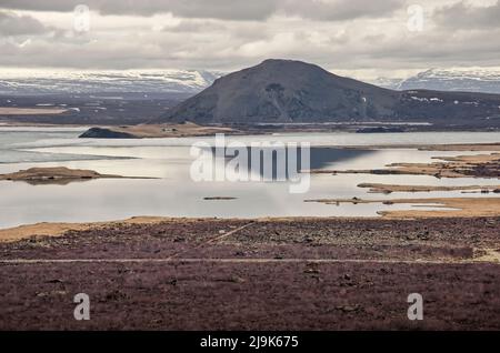 Blick vom Kraterrand des Hverfjall auf den teilweise gefrorenen See Myvatn und den Mount Vindbelgjarfjall unter einem dramatisch bewölkten Himmel Stockfoto