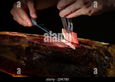 Schneiden von spanischem íberic Schinken. Spanischer Jamon und traditionelles Essen. Trockener spanischer Schinken, Jamon Serrano, Bellota, italienischer Prosciutto Crudo oder Parmaschinken. Stockfoto