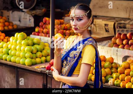 indische kaukasische Frau in traditionellem Kleid.hindu Modell golden Kundan Schmuck-Set bindi Ohrringe und Nasenringpiercing nath Auswahl Früchte Shopper Stockfoto