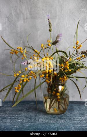 Frühlingsblumen in einem Glas. Einfache Komposition Stillleben mit Akazie und Lavendelblüten. Hellgrauer Hintergrund mit Kopierbereich. Stockfoto