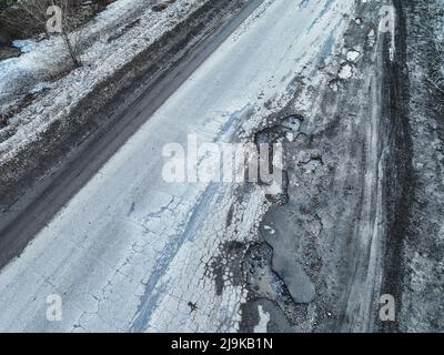 Gebrochene alte Asphaltstraße außerhalb der Stadt. Gruben und Schlaglöcher. Luftaufnahme Stockfoto