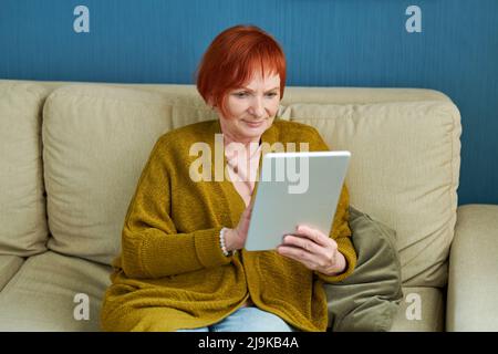 Porträt einer lächelnden, reifen Frau, die zu Hause ein digitales Tablet auf dem Sofa benutzt Stockfoto