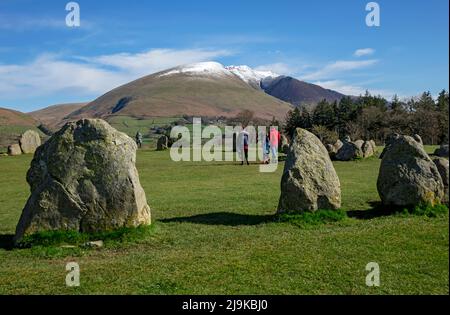 Die Besucher wandern am Castlerigg Stone Circle, der im Frühling im späten Winter im Lake District National Park England über dem schneebedeckten Blencathra liegt Stockfoto