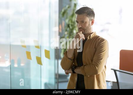 Geschäftsmann Denken Blick Auf Haftnotizen Auf Glas Im Büro Stockfoto