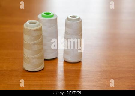 Rollen mit weißen Fäden für eine Nähmaschine auf einem polierten Holztisch im Werker Stockfoto