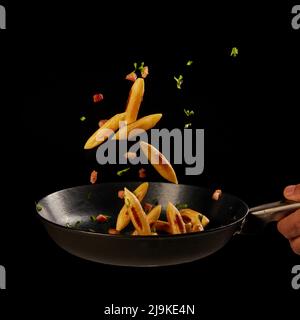 Österreichische und deutsche Pasta-Spezialität genannt Schupfnudeln in einer Pfanne mit einer Hand auf schwarzer Oberfläche Stockfoto