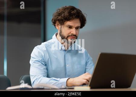Ein Geschäftsmann, der im Büro einen Laptop benutzt, sitzt auf einem Stuhl Stockfoto